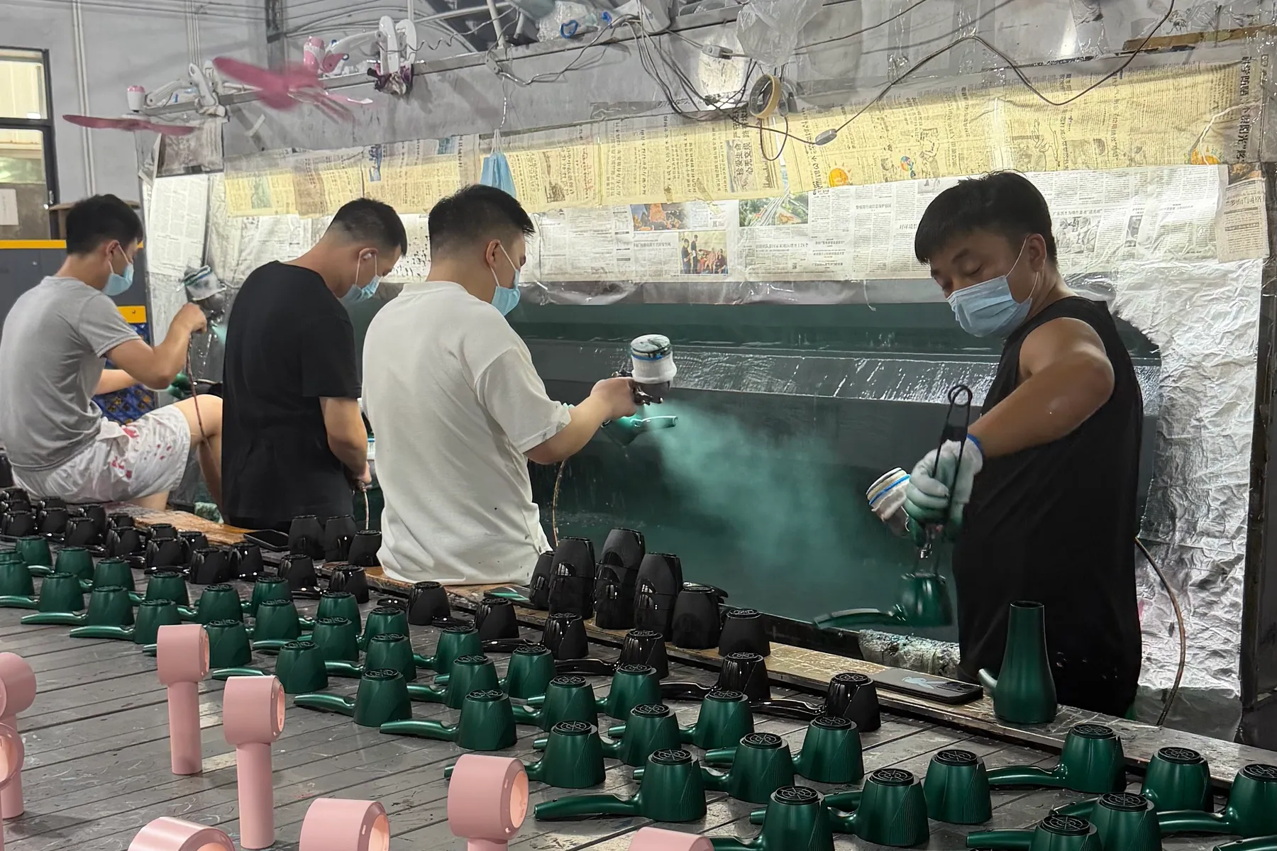 Workers spray coating green, black and pink custom hair dryer housings in production