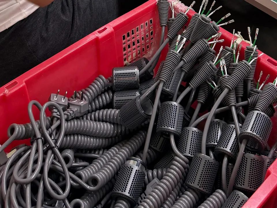 Coiled hair dryer power cords and electrical connection components in a production bin