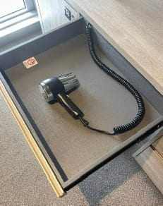 Existing hotel hair dryer and coiled cord stored in an open drawer