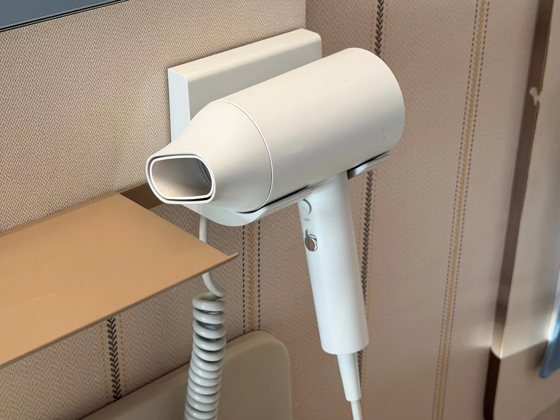 Handheld hotel hair dryer stored in a fixed wall holder with a coiled cord
